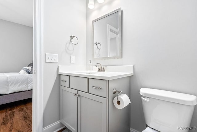 bathroom with toilet, ensuite bath, wood finished floors, vanity, and baseboards