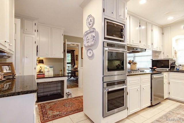 kitchen with appliances with stainless steel finishes, light tile patterned flooring, white cabinetry, under cabinet range hood, and dark stone counters