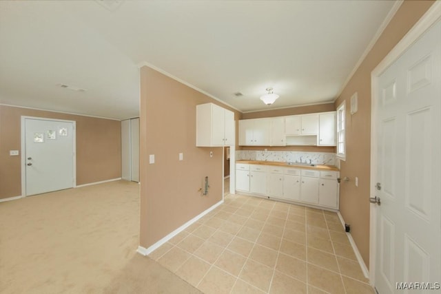 kitchen featuring baseboards, white cabinetry, crown molding, and light countertops