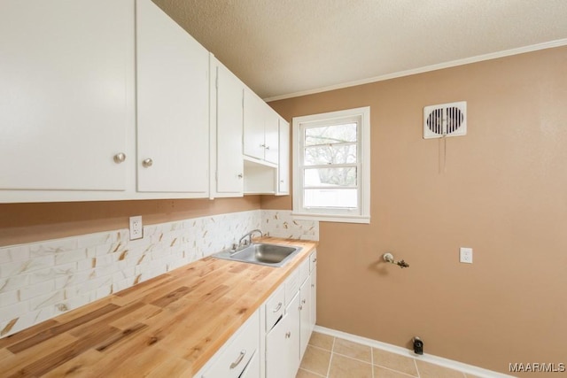 washroom with cabinet space, a textured ceiling, baseboards, light tile patterned floors, and crown molding
