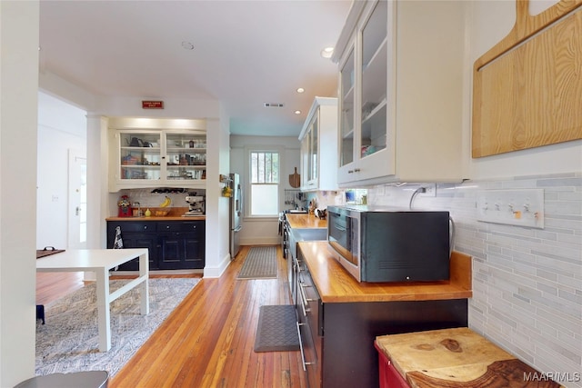 1207 Woodward Ave, Montgomery, AL 36106 - kitchen featuring stainless steel microwave, light wood finished floors, tasteful backsplash, butcher block counters, and glass insert cabinets