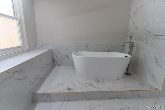 full bathroom with marble finish floors, a freestanding bath, a wainscoted wall, and tile walls