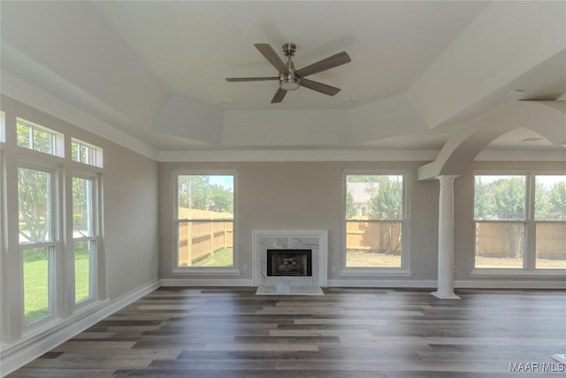 unfurnished living room featuring a raised ceiling, decorative columns, a high end fireplace, a ceiling fan, and arched walkways