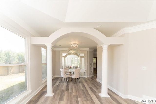 dining space featuring ornate columns, arched walkways, wood finished floors, crown molding, and baseboards
