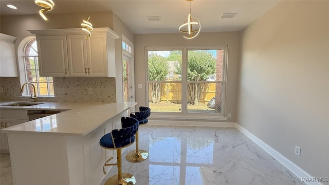 kitchen with a sink, light marble finish flooring, light countertops, backsplash, and baseboards