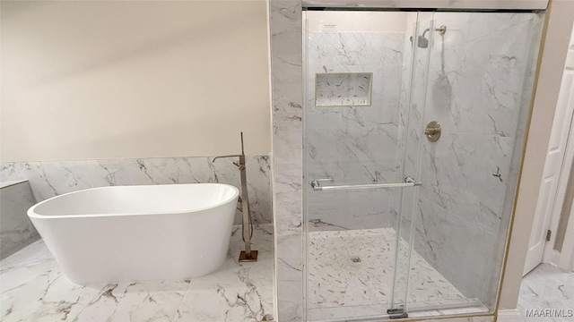 full bathroom featuring marble finish floors, a freestanding bath, wainscoting, a marble finish shower, and tile walls