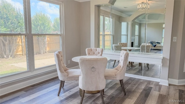 dining area featuring arched walkways, baseboards, wood finished floors, crown molding, and decorative columns