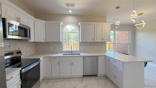kitchen featuring stainless steel appliances, light marble finish flooring, a peninsula, a sink, and decorative backsplash
