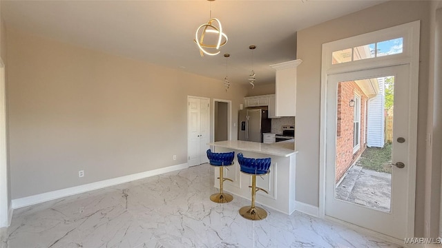 kitchen featuring appliances with stainless steel finishes, white cabinets, a kitchen bar, light countertops, and baseboards