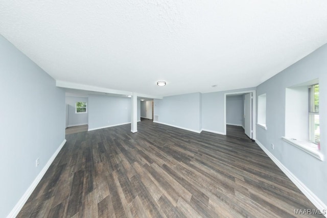unfurnished living room featuring dark wood-style flooring, baseboards, and healthy amount of natural light