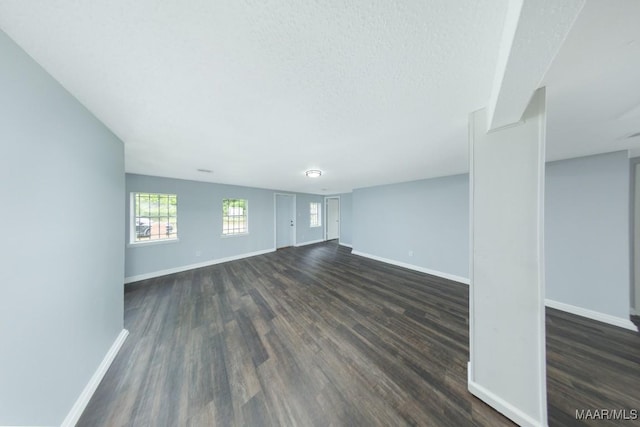unfurnished living room with dark wood-type flooring, baseboards, and a textured ceiling