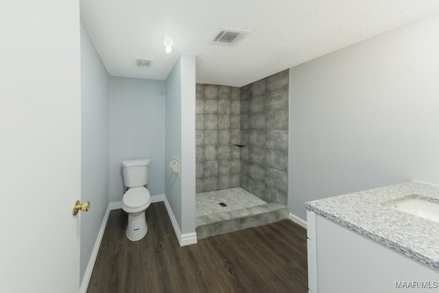 bathroom with wood finished floors, baseboards, a tile shower, toilet, and vanity