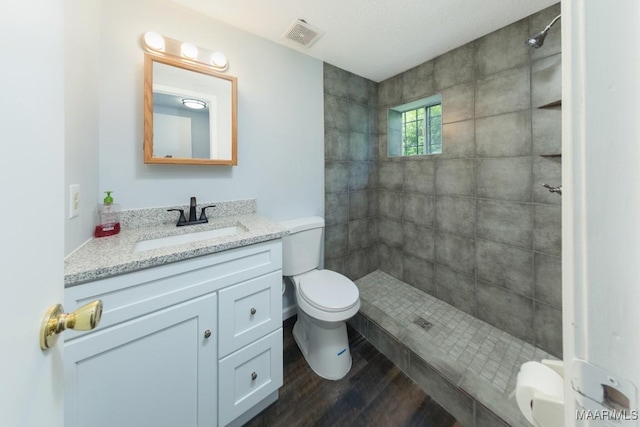 full bathroom featuring toilet, a tile shower, vanity, and wood finished floors