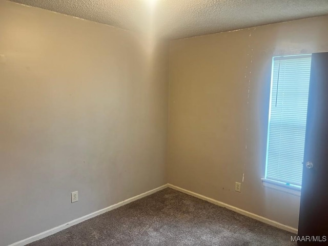 empty room with a textured ceiling, dark colored carpet, and baseboards