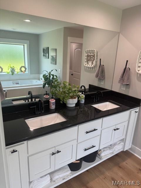 bathroom featuring wood finished floors, double vanity, a tub, and recessed lighting