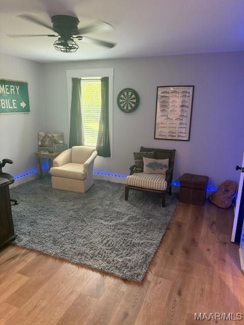 living area featuring wood finished floors, a ceiling fan, and baseboards