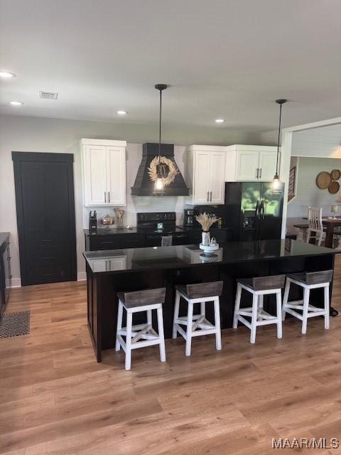 kitchen featuring black appliances, premium range hood, dark countertops, white cabinetry, and light wood-style flooring