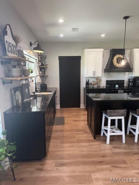 kitchen featuring premium range hood, black range oven, dark countertops, a sink, and white cabinetry