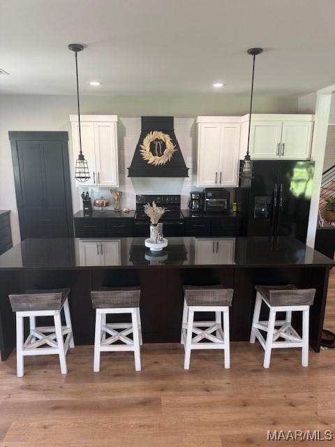 kitchen featuring black appliances, custom range hood, dark countertops, white cabinets, and a kitchen breakfast bar
