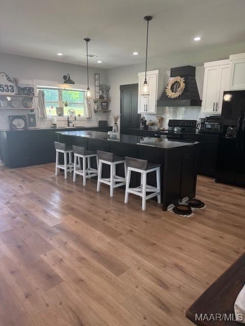 kitchen with black appliances, custom exhaust hood, dark countertops, a center island, and white cabinetry