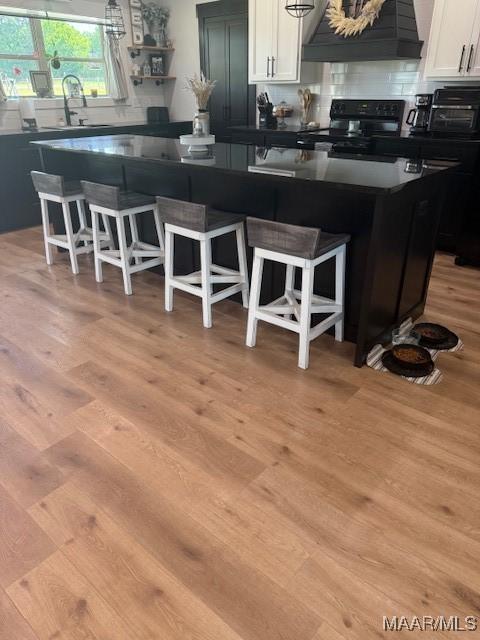 kitchen featuring black range with electric cooktop, custom range hood, dark countertops, and white cabinetry
