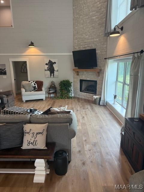 living room featuring healthy amount of natural light, a high ceiling, a brick fireplace, and wood finished floors