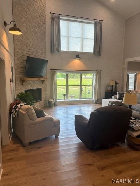 living room with high vaulted ceiling, wood finished floors, plenty of natural light, and a fireplace