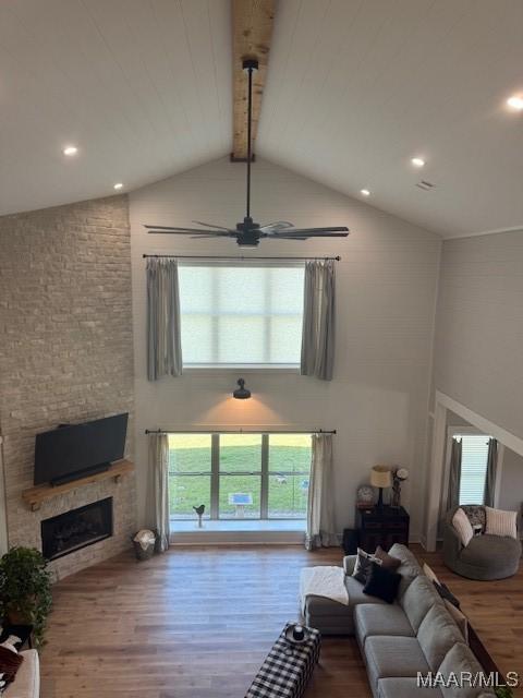 living area with wood finished floors, high vaulted ceiling, beamed ceiling, a fireplace, and ceiling fan