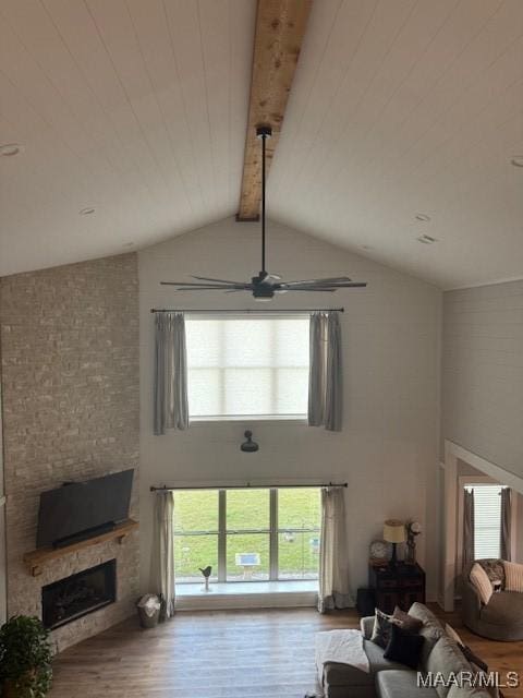 living area with wood finished floors, a large fireplace, beam ceiling, a ceiling fan, and plenty of natural light