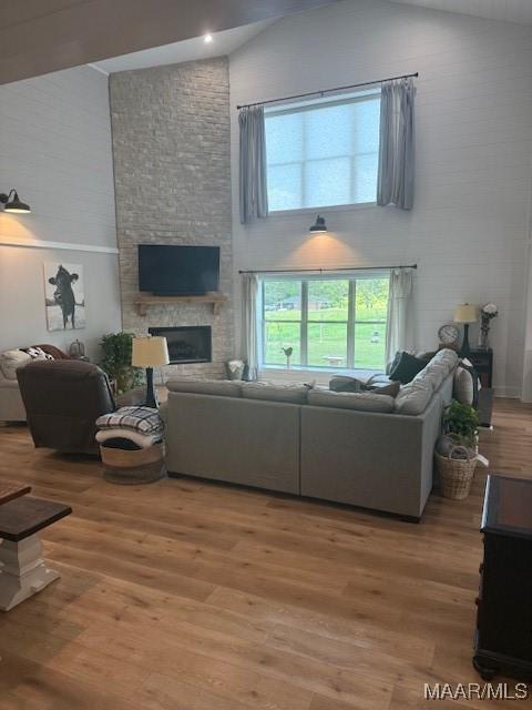 living area featuring high vaulted ceiling, light wood-type flooring, and a fireplace