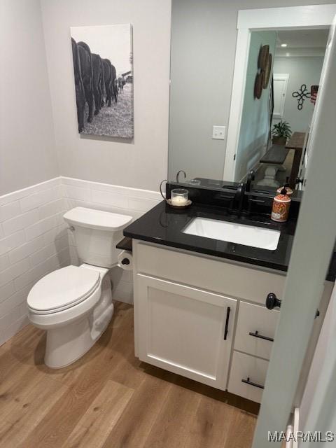 half bath featuring wood finished floors, a wainscoted wall, toilet, vanity, and tile walls