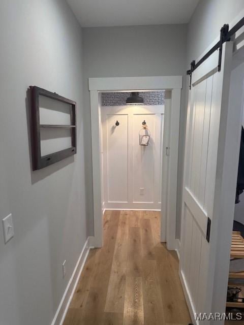 hallway featuring a barn door, light wood finished floors, and baseboards