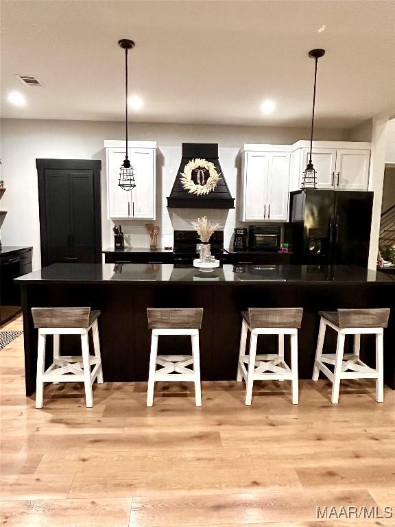 2533 Weldon Rd, Tallassee, AL 36078 - kitchen with black fridge with ice dispenser, premium range hood, dark countertops, white cabinetry, and a kitchen breakfast bar