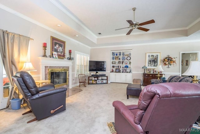 carpeted living room with ceiling fan, a high end fireplace, ornamental molding, and a tray ceiling