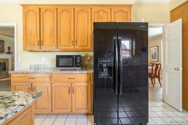kitchen with black fridge with ice dispenser, crown molding, stainless steel microwave, light stone counters, and light tile patterned floors