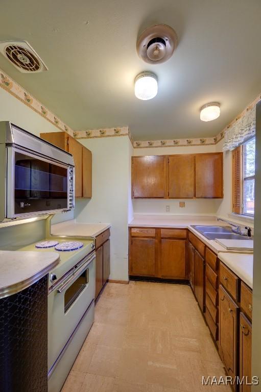 205 9th Ave, Selma, AL 36701 - kitchen with white electric range, stainless steel microwave, light flooring, brown cabinets, and light countertops