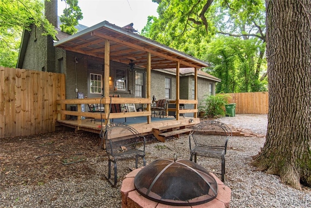 back of property with a fire pit, fence, a wooden deck, brick siding, and a chimney