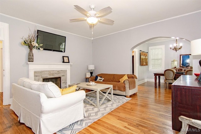 living area featuring arched walkways, wood finished floors, ceiling fan, a tiled fireplace, and a chandelier