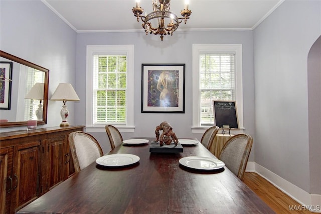 dining room with a chandelier, wood finished floors, arched walkways, baseboards, and ornamental molding