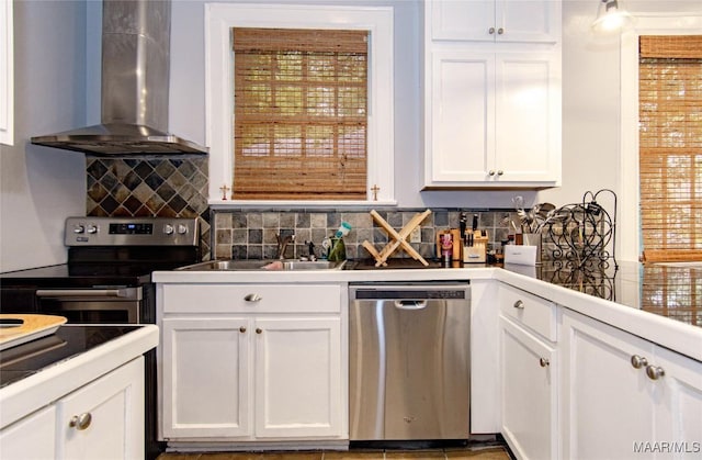 kitchen featuring stainless steel appliances, wall chimney range hood, a sink, and white cabinetry