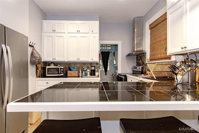 kitchen with stainless steel appliances, dark countertops, wall chimney exhaust hood, tasteful backsplash, and a breakfast bar area