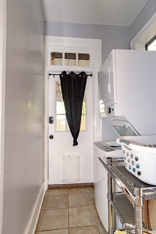 washroom featuring stacked washer / dryer, baseboards, and light tile patterned flooring