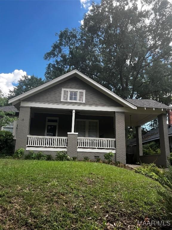 bungalow-style home with covered porch, a front lawn, and brick siding