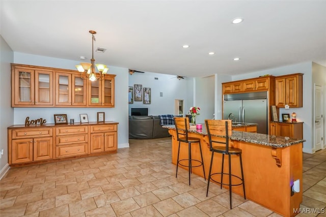 kitchen with stainless steel built in refrigerator, brown cabinets, a breakfast bar, dark stone counters, and recessed lighting