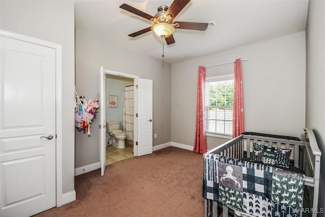 carpeted bedroom featuring a crib, baseboards, ensuite bath, and ceiling fan
