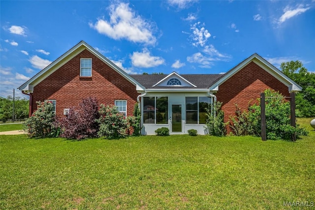 view of front of home with a front yard, brick siding, and a sunroom