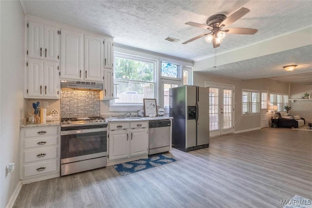 kitchen with stainless steel appliances, under cabinet range hood, a textured ceiling, open floor plan, and light wood-type flooring