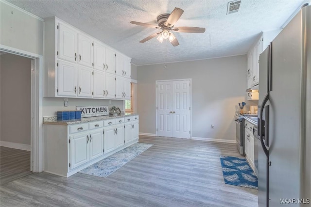 kitchen featuring freestanding refrigerator, a textured ceiling, white cabinetry, light wood-type flooring, and light countertops