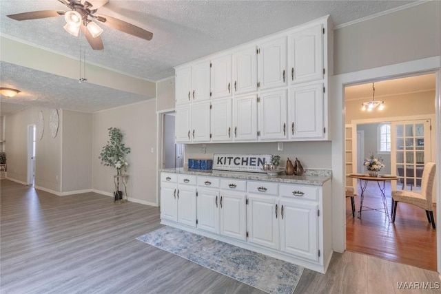 kitchen with a textured ceiling, light wood finished floors, white cabinetry, ornamental molding, and ceiling fan