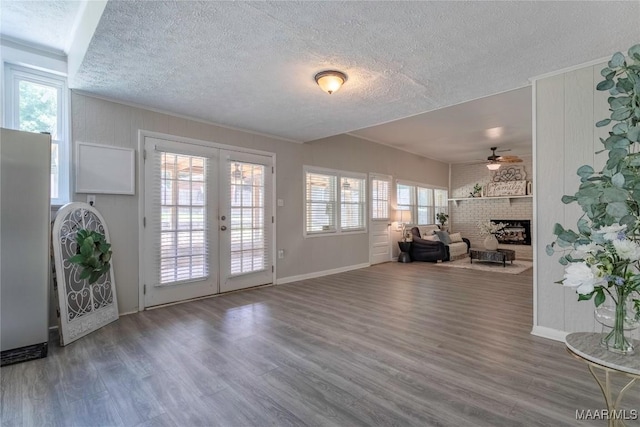 unfurnished living room featuring a textured ceiling, ceiling fan, a fireplace, wood finished floors, and french doors